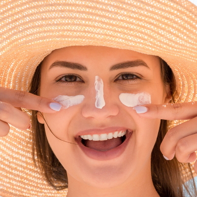 Femme avec chapeau de paille s'appliquant de la crème solaire.