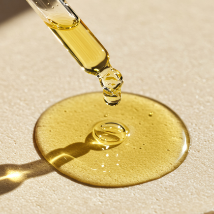 Une pipette qui dépose une goutte de sérum sur une surface beige