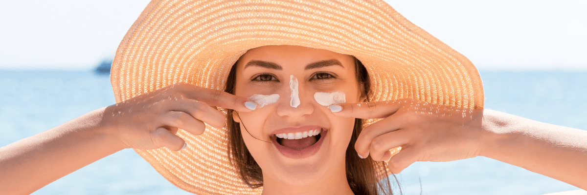 Femme avec chapeau de paille s'appliquant de la crème solaire.