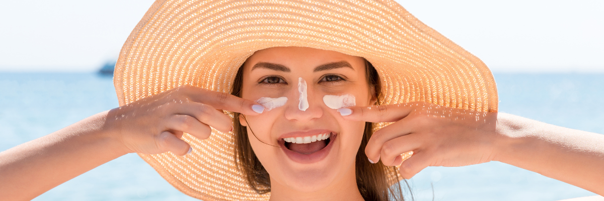 Femme avec chapeau de paille s'appliquant de la crème solaire.