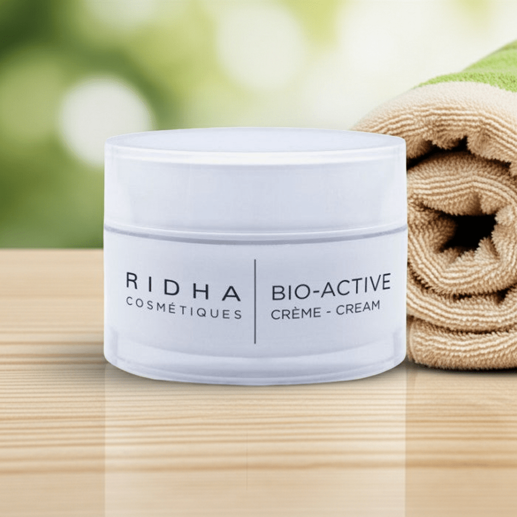 Pot de crème Bio-Active Ridha Cosmétiques déposé sur une table  en bois clair avec une serviette roulée beige.