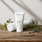 Un tube de masque aromatique de Ridha Cosmétiques déposé sur une surface en bois avec une serviette roulée et des branches vertes